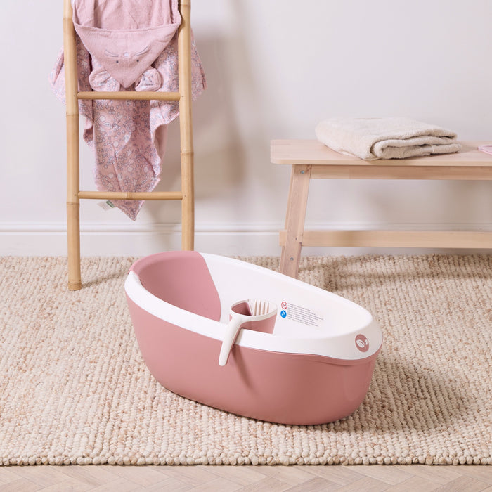 Nati Baby Bath in shell with coordinating  jug, styled on a textured nursery rug with soft pink and natural wood accents.