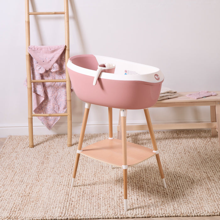 Nati Baby Bath in shell displayed on wooden stand with matching jug, showcasing elevated bathing setup and compact storage shelf.