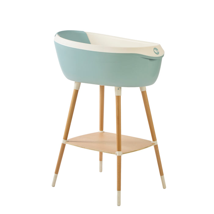 Angle view of the Nati Baby Bath in blue on a wooden stand, in a white background.