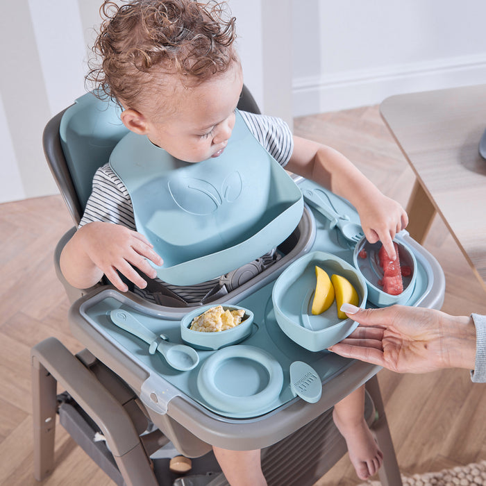 A child in the Nova Maison highchair with the accessory pack, eating fruit with a bib on.