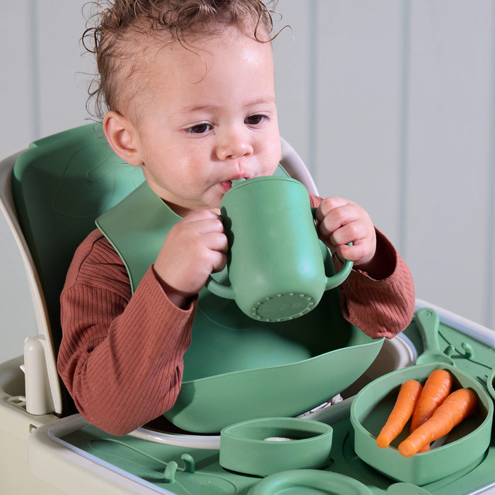 A baby drinking from a sip cup comfortably and eating in the Nova Maison highchair, with the green and white accessory pack showcased.