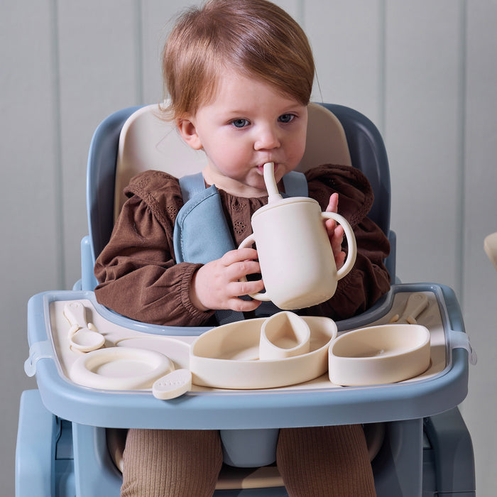 A child drinking from a sip cup while sitting in the Nova Maison highchair, with the accessory tableware set displayed.