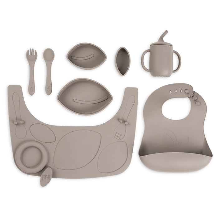Flat lay cutout of the Nova highchair accessory pack in cocoa, including silicone bib, divided bowls, cup, spoon and fork.