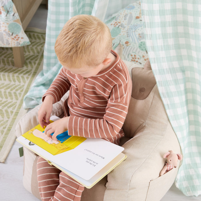 Toddler reading a picture book beneath the Good Life nursery canopy, seated in a beanbag chair