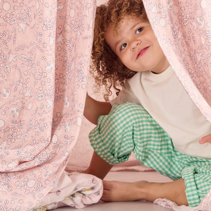 Smiling child peeking through the Tiny Tails floral canopy fabric, creating a playful and cosy hideaway corner.