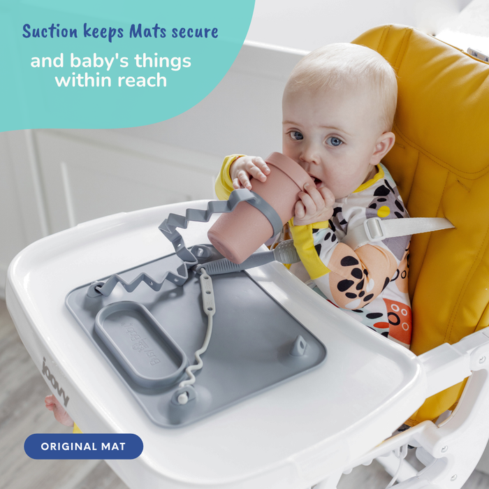 baby sitting in high chair drinking a cup attached to busy baby suction placemat with bottle bungee