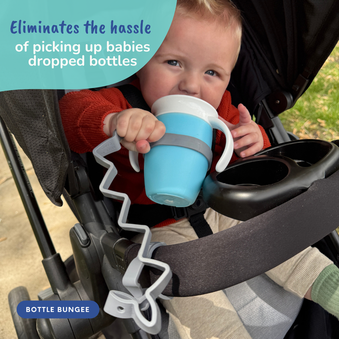 baby in stroller drinking out of cup attached to stroller handle with busy baby bottle bungee