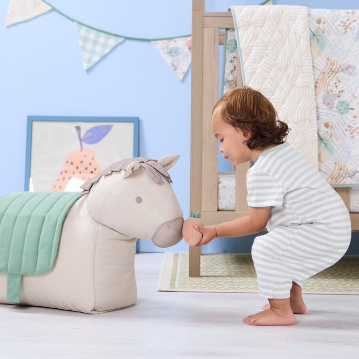 Toddler feeding carrot toy to Ride-On Henry Horse beanbag, showing playful interaction and soft green saddle in a cosy nursery
