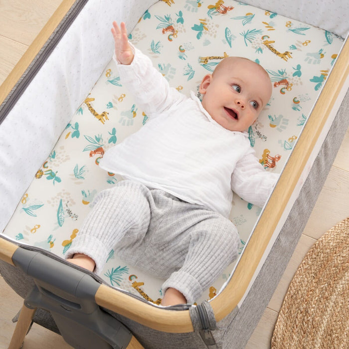 Baby lying on Run Wild bedside crib fitted sheet, organic cotton with playful jungle animal prints offering softness and a snug fit