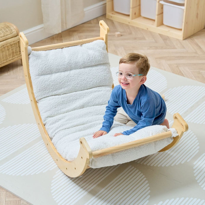 Smiling child seated on the Scala Pikler with boucle natural cushion, highlighting comfortable design and Montessori-inspired play