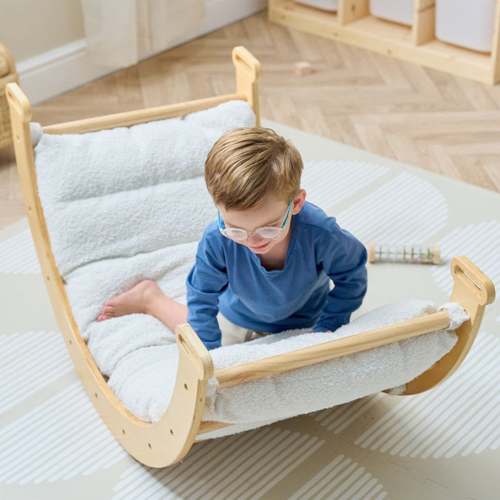 Young child climbing on the Scala Pikler with boucle natural cushion, showing supportive padding and safe, open-ended play