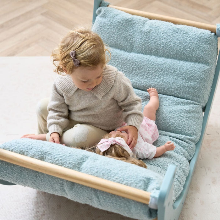 Top-down view of toddler playing gently with a soft toy doll on the ocean stone cushion