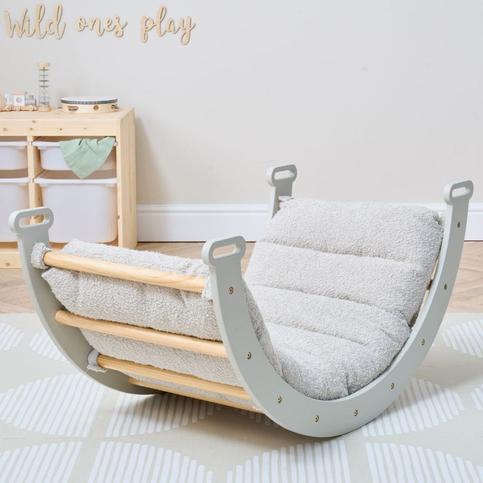 Nursery room view of Scala Montessori Pikler Cushion in Boucle Mushroom secured to rocking frame, styled with natural wood and soft tones