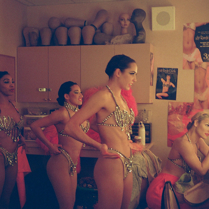 A close-up photograph of four performers backstage Three women in sequined bikinis stand while another applies makeup