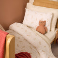 Children's bed with Love Cats patterned bedding and a teddy bear, against a brown wall.