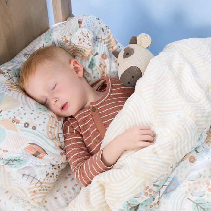 Toddler sleeping peacefully under the Good Life duvet and pillowcase set with farmyard print, featuring soft muslin fabric and cosy warmth