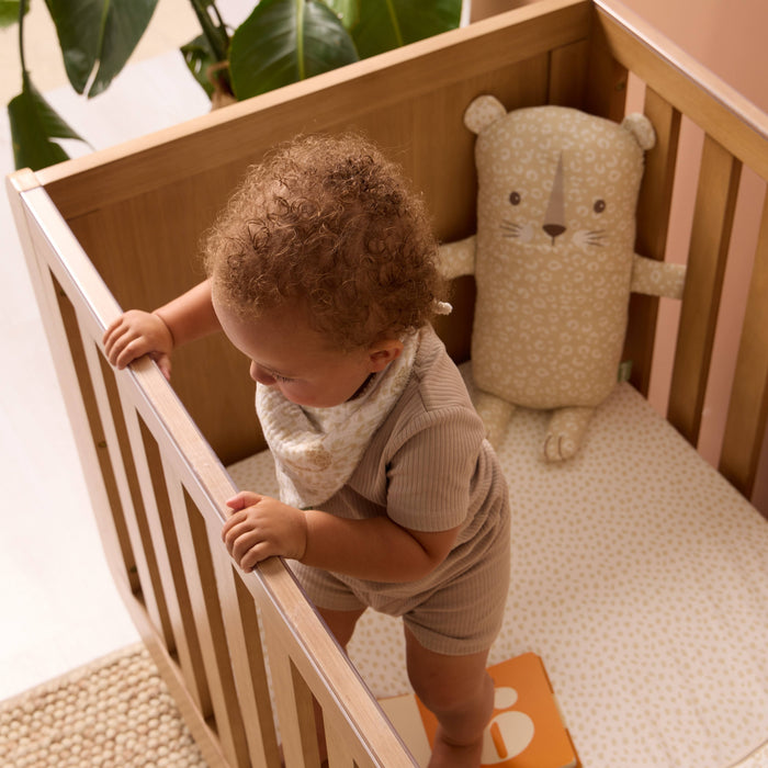 A child is standing in a cot bed with Larry the leopard pillow in the background