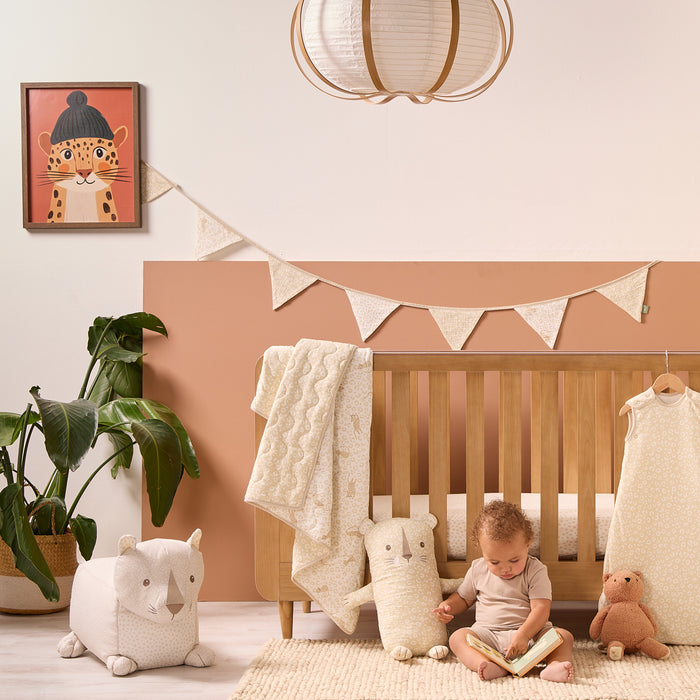 Soft Leopard Cuddle Cushion styled in a warm neutral nursery beside a wooden cot, adding soft playful charm to the space