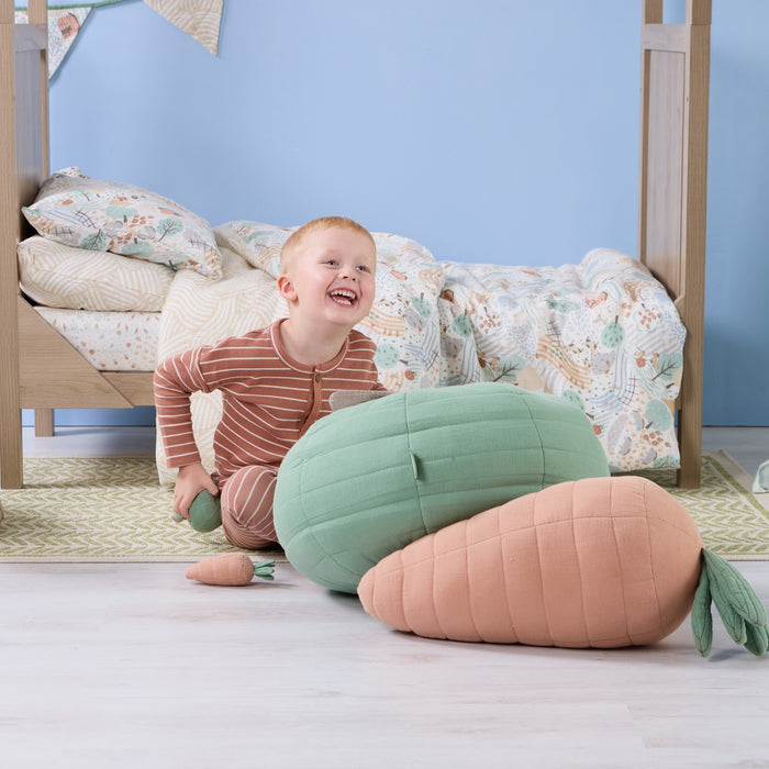 Smiling toddler playing beside the Soft Muslin Apple Cushion, showing its plump quilted shape and soft tactile muslin fabric