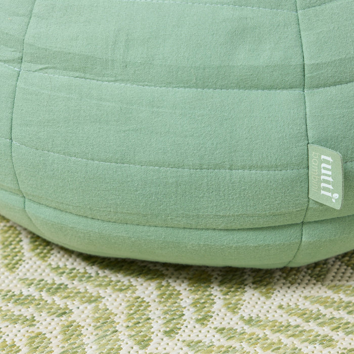 Close-up of the Soft Muslin Apple Cushion showing quilted green muslin texture with Tutti Bambini fabric label detail on side seam