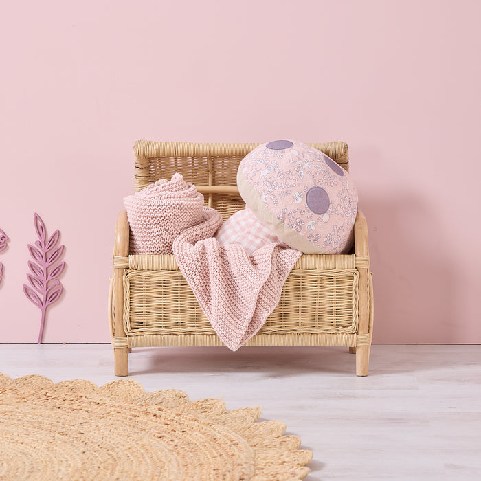 Soft Muslin Mushroom Cushion styled in a pink nursery, resting on a wicker bench with knitted blankets for a cosy decorative touch