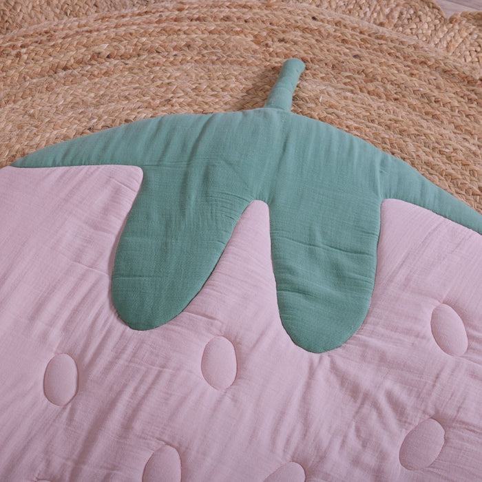 Close-up of strawberry-shaped muslin baby playmat showing green leaf detail and soft quilted pink fabric.