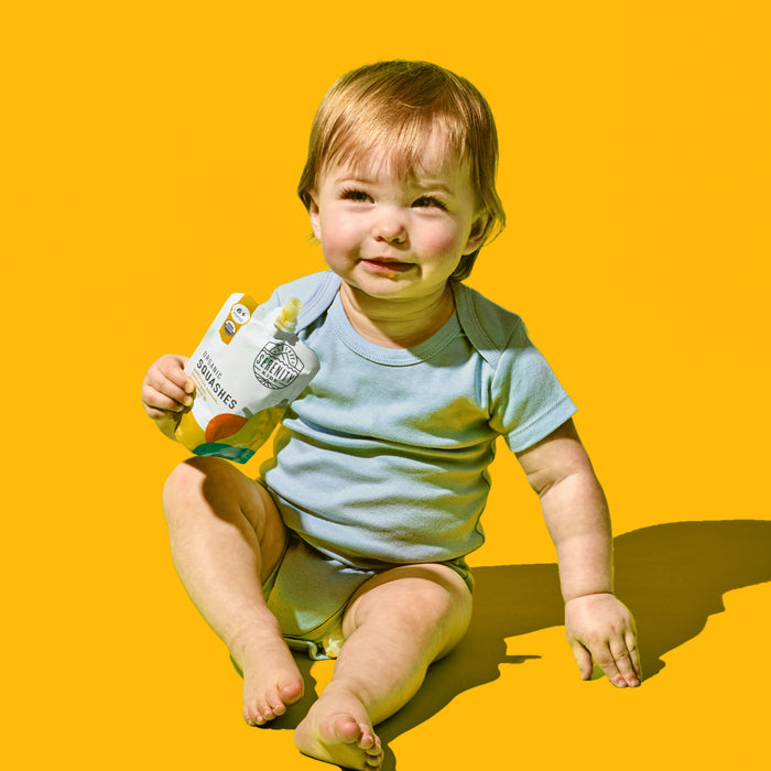 Child holding squash baby food against a yellow background