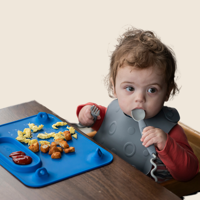 Baby eating at table with Blue Busy Baby Mat silicone mat with Busy Baby Utensils