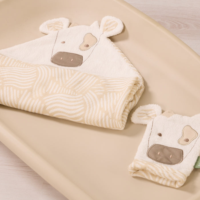 Clemi the Cow hooded towel and matching wash mitt folded neatly together, featuring cow face embroidery and beige patterned towel edging