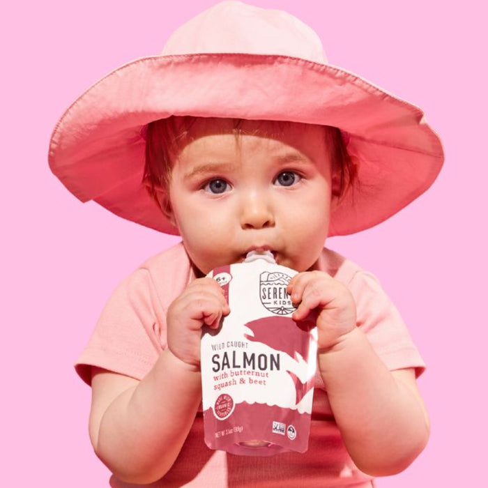 Baby holding a pink pouch with 'Seren' branding against a pink background