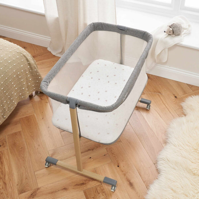 Top view of ZiZee Essential Crib in Oak and Charcoal colours, featuring a mesh surrounding, a white mattress, and wooden legs, placed next to a fluffy white rug.